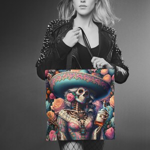 May include: A tote bag with a colorful illustration of a skeleton wearing a sombrero and holding a bottle of tequila. The skeleton is surrounded by flowers and has a skull face with a painted design.