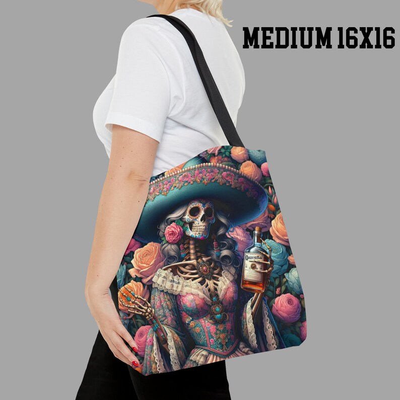 May include: A tote bag with a colorful illustration of a skeleton woman wearing a sombrero and holding a bottle of tequila. The background is filled with pink, blue, and yellow flowers.