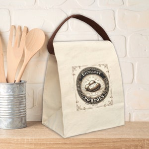 May include: A beige canvas lunch bag with brown handles. The bag has a black and white graphic of potatoes with the text "Excellent Potatoes" in a decorative frame.