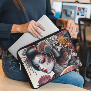 May include: A laptop sleeve with a colorful geisha design. The sleeve is black with a white background and features a geisha with red and blue flowers. The geisha has black hair and is wearing a red and white kimono.