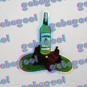 May include: Holographic sticker featuring a green Jameson Irish Whiskey bottle atop a brown saddle with a star. The sticker has a green and blue border and is on a white background. The sticker is a fun, whimsical design.