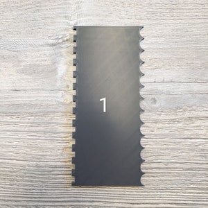 May include: A black plastic cake decorating tool with a scalloped edge and the number "1" printed on the front.