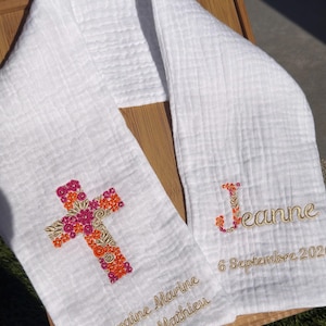May include: White baptismal scarf with embroidered cross and name. The cross is decorated with orange, pink, and gold floral designs. The name "Jeanne" and date "6 Septembre 2020" are also embroidered.