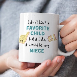 May include: White ceramic coffee mug with a blue and yellow design. The mug reads "I don't have a favorite child but if I did, it would be my niece".