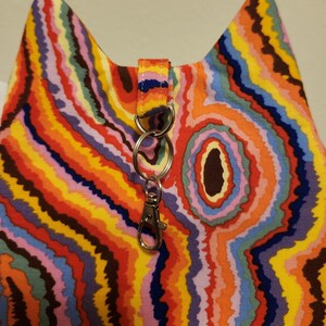 May include: A colorful fabric cat ear bag with a rainbow swirl pattern and a silver key chain attached.