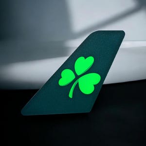 May include: A dark green airplane tail fin with a bright green four-leaf clover design.