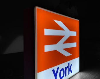 May include: A bright orange and white sign with a stylized train track symbol and the word "York" in blue letters.