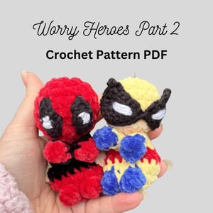 May include: Two small, handmade crochet figures of superheroes, one red and black, the other yellow and blue, are held in a hand. The text "Worry Heroes Part 2 Crochet Pattern PDF" is above the figures.