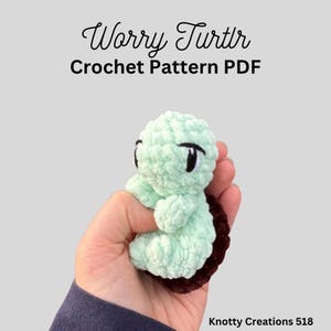 May include: A crocheted Worry Turtle in light green with black eyes and a brown shell is held in a hand. The text "Worry Turtle Crochet Pattern PDF" is above the turtle. The creator's name, Knotty Creations 518, is at the bottom.