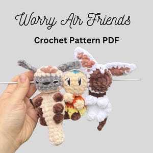 May include: Three small plush figures made of soft yarn, including a beige and brown creature with long ears, a central character with a blue arrow on its head, and a white and brown creature with large ears. Text reads Worry Air Friends Crochet Pattern PDF.