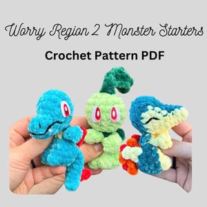 Puede incluir: Tres pequeños monstruos de peluche hechos de hilo suave. El monstruo azul tiene ojos rojos, el verde claro tiene ojos rojos y un brote, y el azul y amarillo tiene detalles naranjas. El texto dice: Worry Region 2 Monster Starters Crochet Pattern PDF.