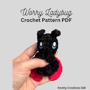 May include: A black and red crocheted ladybug with blue eyes is held in a hand. The ladybug has a rounded body and small antennae. Text above reads "Worry Ladybug Crochet Pattern PDF."