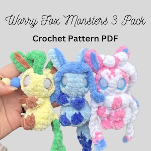 May include: Three crocheted Worry Fox Monsters in yellow, blue, and pink. Each has large eyes and a unique color scheme. The text "Worry Fox Monsters 3 Pack" and "Crochet Pattern PDF" are displayed above the toys.