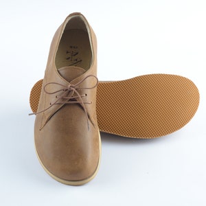 Puede incluir: Un par de zapatos marrones de cuero con cordones y suela texturizada. Los zapatos tienen un dise&ntilde;o sencillo y est&aacute;n hechos de cuero suave y flexible.