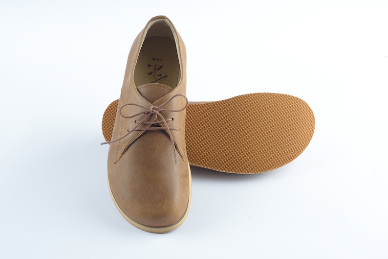 Puede incluir: Un par de zapatos marrones de cuero con cordones y suela texturizada. Los zapatos tienen un dise&ntilde;o sencillo y est&aacute;n hechos de cuero suave y flexible.