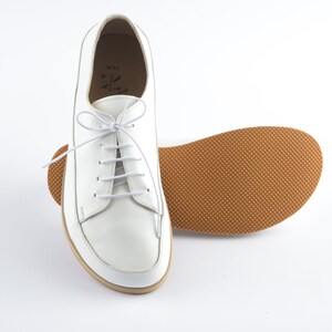 May include: White leather lace-up shoes with a brown rubber sole. The shoes have a simple design and are a classic style.