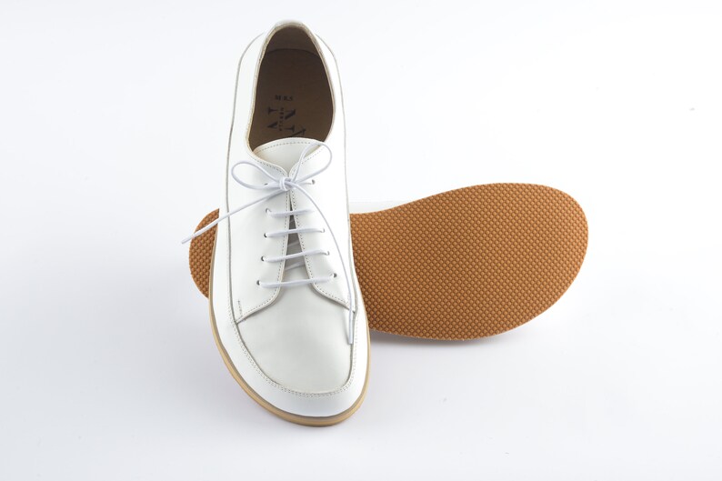 May include: White leather lace-up shoes with a brown rubber sole. The shoes have a simple design and are a classic style.