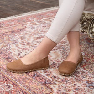 May include: A pair of brown leather ballet flats with a stitched edge. The flats are on a patterned rug.