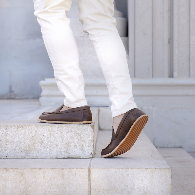 May include: A person wearing white pants and brown leather loafers is walking up a set of stairs.