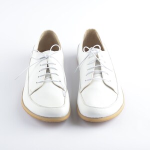 May include: A pair of white leather lace-up shoes with white laces. The shoes have a rounded toe and a low heel.