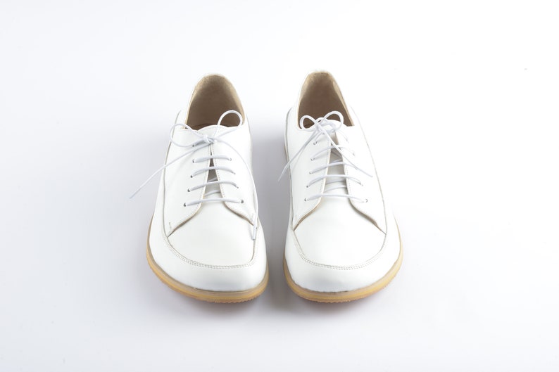 May include: A pair of white leather lace-up shoes with white laces. The shoes have a rounded toe and a low heel.