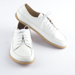 May include: A pair of white leather lace-up shoes with a rounded toe and a cream-colored sole.