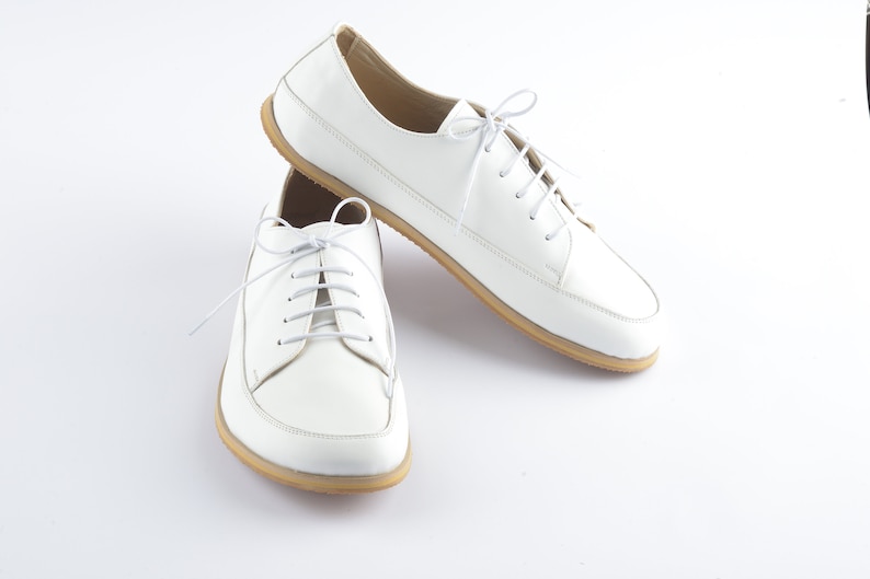 May include: A pair of white leather lace-up shoes with a rounded toe and a cream-colored sole.