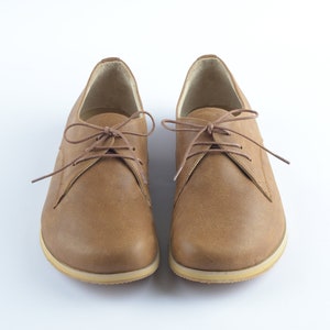 Puede incluir: Un par de zapatos marrones de cuero con cordones y suela de color marr&oacute;n claro.