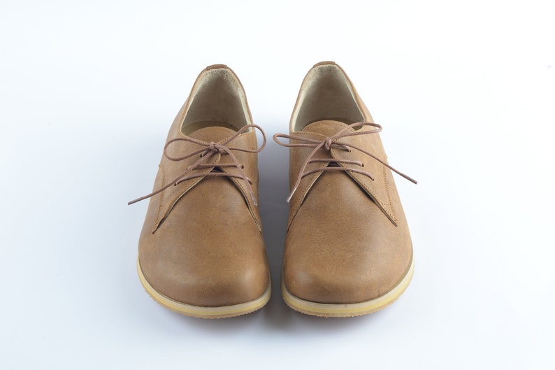 Puede incluir: Un par de zapatos marrones de cuero con cordones y suela de color marr&oacute;n claro.