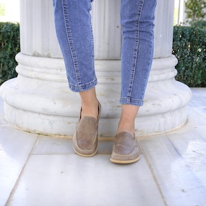 May include: A pair of brown leather loafers with a textured finish. The shoes have a rounded toe and a light-colored sole. The loafers are worn with blue jeans.