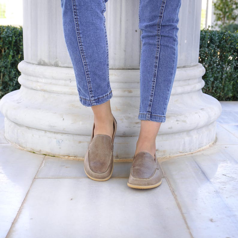May include: A pair of brown leather loafers with a textured finish. The shoes have a rounded toe and a light-colored sole. The loafers are worn with blue jeans.