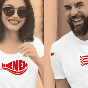 Può includere: Due magliette bianche con grafiche rosse. Una presenta la scritta "BREMEN" in un design stilizzato, l'altra un cuore rosso e un disegno pixelato rosso e bianco. L'immagine mostra due persone che indossano le magliette.