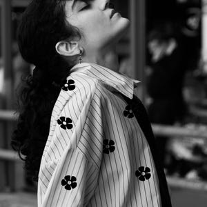 May include: A black and white photo of a person wearing a striped shirt with black floral embroidery. The person is looking up and has their head tilted back.