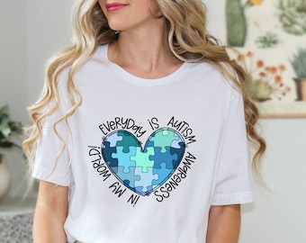 May include: White t-shirt with a blue and green puzzle piece heart design. The text around the heart reads "In my world everyday is autism awareness."