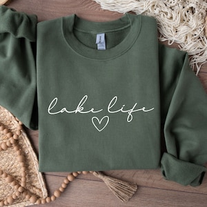 K&ouml;nnte beinhalten: Ein gr&uuml;ner Pullover mit dem Text "lake life" in wei&szlig;er Kursivschrift und einem kleinen wei&szlig;en Herz.