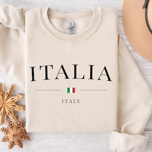 May include: A beige sweatshirt with the word "ITALIA" printed in black, with the Italian flag and the word "ITALY" underneath.