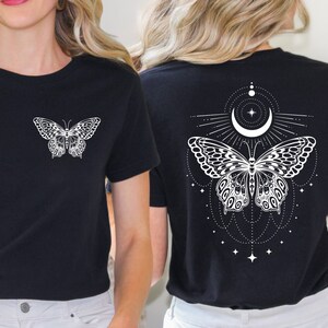 May include: Two black t-shirts featuring a white butterfly design. One shirt has a simple butterfly design on the front, while the other has a more elaborate butterfly design with a crescent moon and stars on the back.