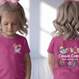 Pu&ograve; includere: Una t-shirt a maniche corte rosa acceso con una piccola grafica sul petto con il nome Emily e il testo Cousin Camp 2026. Il retro mostra una grafica pi&ugrave; grande con il testo Cousin Camp Mama and Papa 2026 e varie icone colorate.