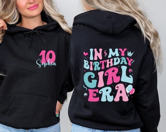 May include: Black hoodie with a pink and blue graphic that says "In My Birthday Girl Era" on the back. The front of the hoodie has a pink number 10 and the name "Sophia" in blue.