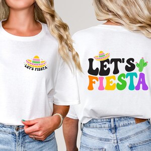 May include: Two white t-shirts with a festive Mexican theme. One shirt features a colorful sombrero and the text "Let's Fiesta". The other shirt features the text "Let's Fiesta" in colorful letters with a cactus.