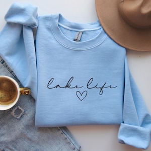 K&ouml;nnte beinhalten: Ein hellblauer Pullover mit dem Schriftzug "lake life" in schwarzer Schrift mit einem kleinen Herz darunter.