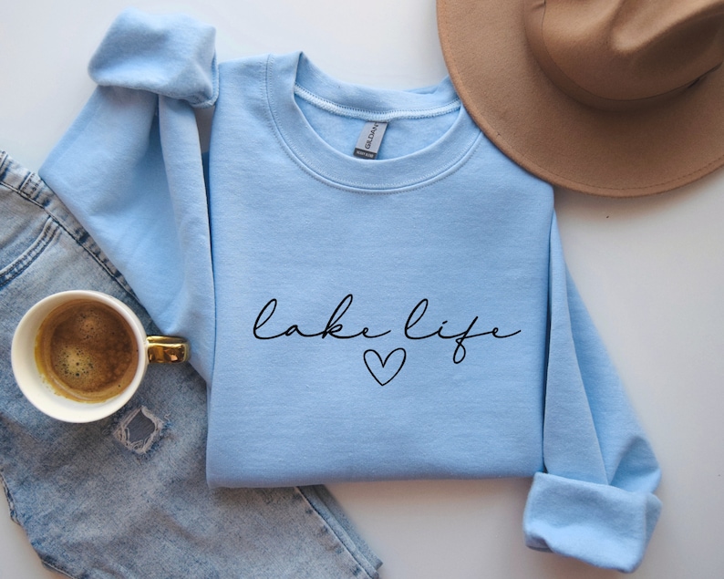 K&ouml;nnte beinhalten: Ein hellblauer Pullover mit dem Schriftzug "lake life" in schwarzer Schrift mit einem kleinen Herz darunter.