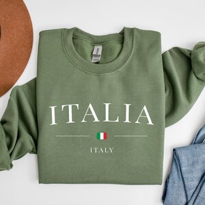 May include: A green sweatshirt with the word "ITALIA" in white letters and the word "ITALY" below it. The Italian flag is between the words.