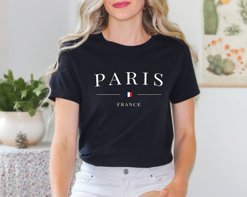 May include: Black t-shirt with white text that reads "PARIS" with a small French flag and the word "FRANCE" underneath.