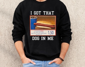 May include: Black sweatshirt with the text "I GOT THAT DOG IN ME." The graphic includes a hot dog, soda, and the price $1.50. The text also includes "1/4 POUND PLUS ALL BEEF HOT DOG AND 20 oz. SODA (With Refill) 580-850 cal."
