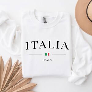 May include: White long-sleeve sweatshirt with the word "ITALIA" in black text and the word "ITALY" in smaller black text below. A small Italian flag is between the words.