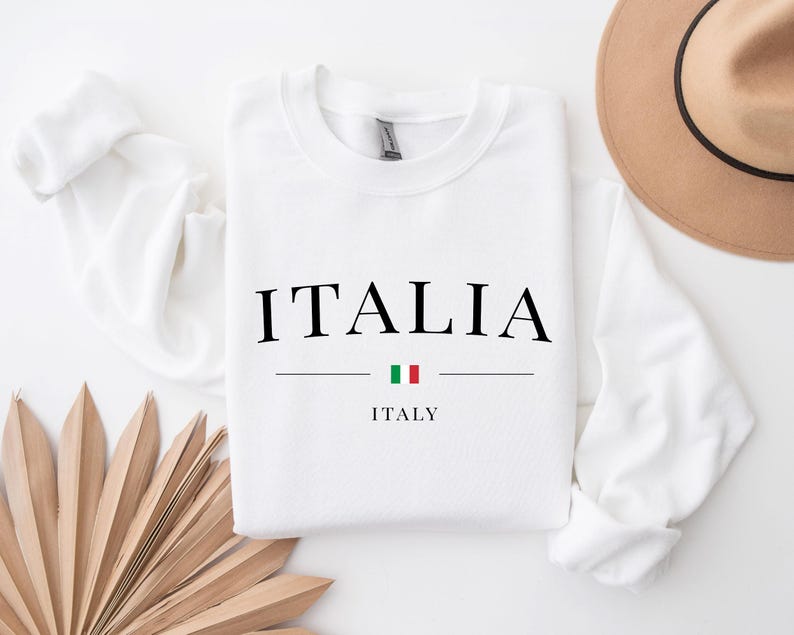 May include: White long-sleeve sweatshirt with the word "ITALIA" in black text and the word "ITALY" in smaller black text below. A small Italian flag is between the words.