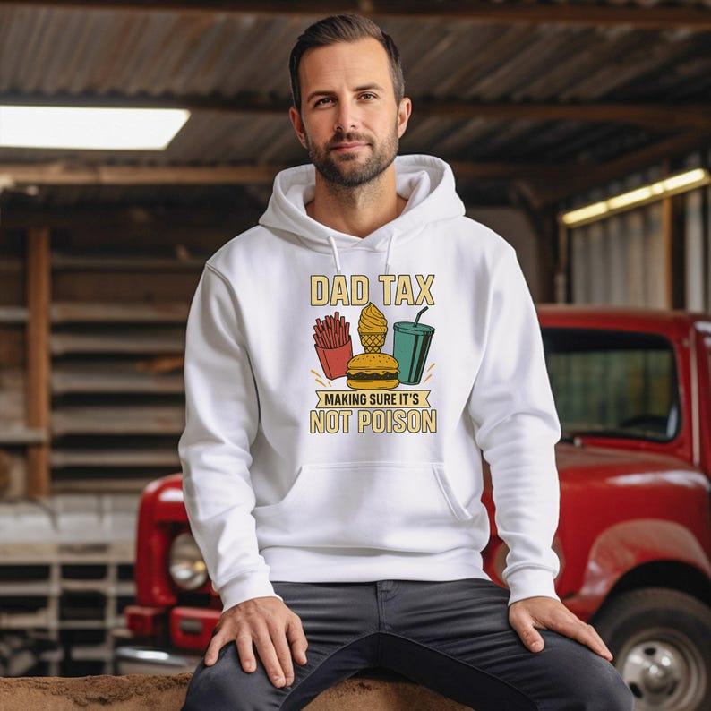 May include: White hoodie featuring the text "DAD TAX" and a graphic of fries, a burger, ice cream, and a drink. The text "MAKING SURE IT'S NOT POISON" is below the graphic. The hoodie is worn by a person.