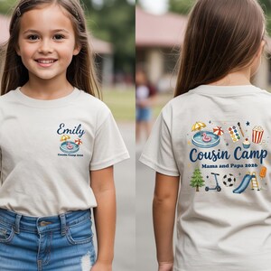 Pu&ograve; includere: Una t-shirt beige a maniche corte con una piccola grafica sul petto sinistro che include il nome Emily e una piscina. Il retro presenta una grande grafica con il testo Cousin Camp, Mama and Papa 2026 e varie icone estive.