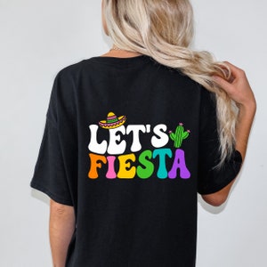 May include: Black t-shirt with a white graphic that says "Let's Fiesta" in rainbow colors. The graphic also includes a cartoon sombrero and cactus.